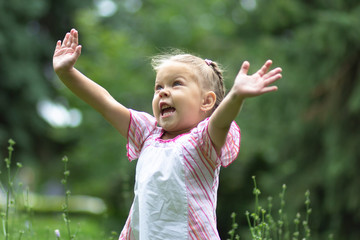 Happy child holding her hands up to sky in the summer park