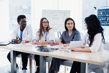 Group of doctors are studying disease patient's history. Team of multiethnic young doctors having a meeting in conference room in the modern bright hospital.