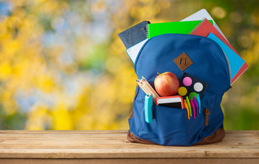 Back to school concept with bag backpack and school supplies on wooden table over autumn bokeh...