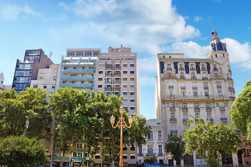 Skyline of historic and modern buildings in Buenos Aires, Argentina, surrounded by green trees, against a blue summer sky.