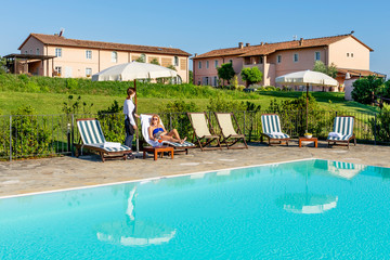 Young waitress serves a poolside cocktail to a customer sitting on a lounger in a resort in the...
