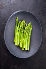 Traditional blanched green asparagus as top view on a cast iron design plate with copy space