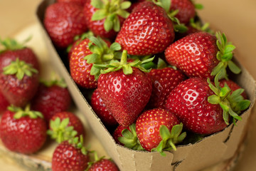 Fresh strawberries in a Kraft box on a wooden stand close-up. Open space, healthy food concept, plants, soil, organic natural products, natural food, vegetarian dishes, vegetables, raw, food festival