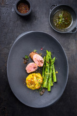 Fried Iberian pork fillet sliced with blanched green asparagus and potato gratin dauphinois with spice as top view on a cast iron design plate