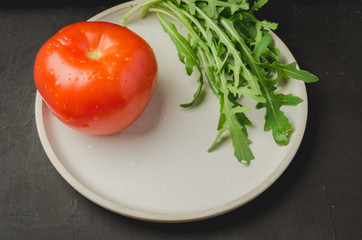 tomato and leaves of arugula in a white bowl against a dark background. Top view