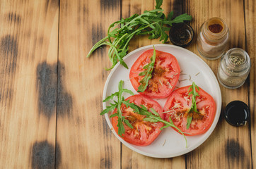 sliced tomatoes and arugula spices salad. In a white bowl on a wooden background. Top view and copy space