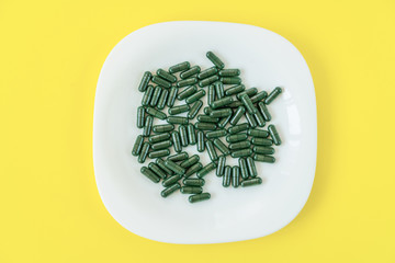 spirulina capsules on a white plate  on yellow, dieting, detox, healthy lifestyle concept
