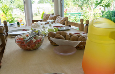 Festive table served dishes and decorated. Lunch in the open air. Orange pitcher of water and flowers. Salad and food in the garden.
