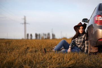 A young girl is traveling around the city hitchhiking. A beautiful young girl went on vacation. A female student in a cowboy hat on the road in autumn.