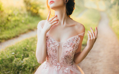gentle elegant photo of girl with fair skin and dark hair, cute slender lady with bare shoulders twisted off straps of pink peach shiny dress, princess touches long neck with slender fingers, no face © kharchenkoirina