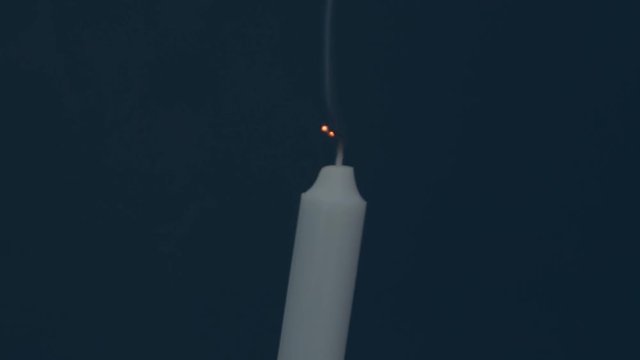 Close up of candle on black. Dying out the flame of a white candle. Smoke from the wick. Blowing out white wax candle in a dark room.