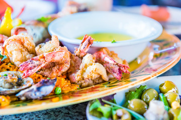 Macro closeup of fried seafood on plate with garlic butter bowl, shrimp, olive salad, rice on platter
