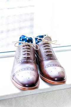 Men's leather new brown shoes closeup still life isolated with blue polka dot socks, watch, shoelaces laces tied, wedding or interview preparation, belt on windowsill in room with window blinds