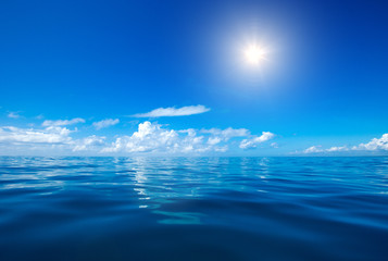 clouds on blue sky over calm sea with sunlight reflection