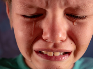 Face of crying boy close up. Eyes, eyelashes, eyebrows, lips, teeth and tears. Emotions and grimaces of upset child
