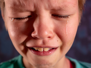 Face of crying boy close up. Eyes, eyelashes, eyebrows, lips, teeth and tears. Emotions and grimaces of upset child