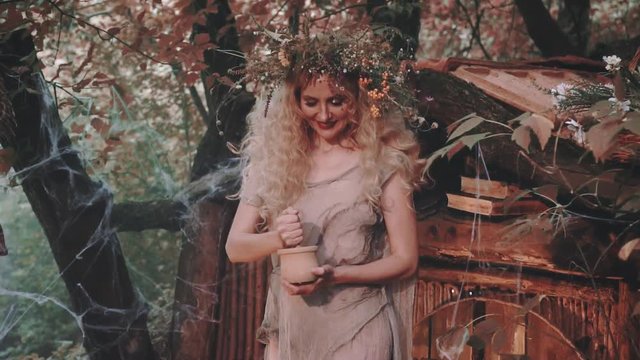 image of crazy old lady with blond curly hair, mysterious fortune-teller mixes ingredients in wooden mortar at little forest house, heathen woman with floral wreath preparing to perform ritual