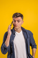 Handsome young man using his phone with smile while standing against yellow background.Young adult man talking on the phone scared in shock with a surprise face, afraid and excited with fear expressio