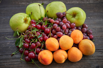 Home garden harvest in the summer, organic fruits, full of nutrients and vitamins, pile of riped apples, peaches, sour cherries and gooseberies on the dark wooden table just after to be harvested.