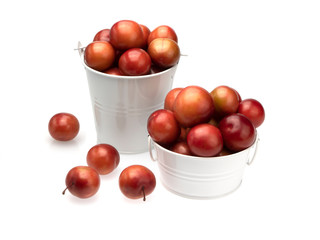 Ripe maroon plums in a white basin, white bucket and scattered near it on a white background. Isolated. Close-up. Still life.