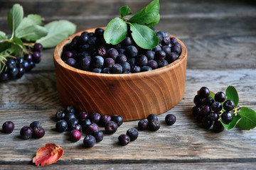 Black chokeberry in wooden utensils on old wooden boards.