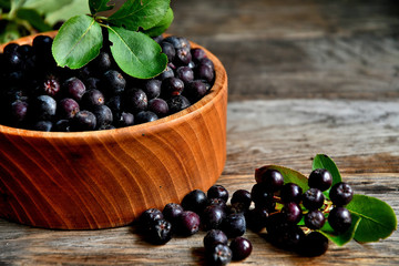 Black chokeberry in wooden utensils on old wooden boards.