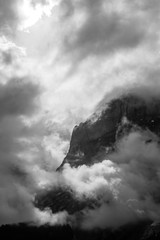 Black and white photo of high Alps mountains and white cloudy sky with sunlight