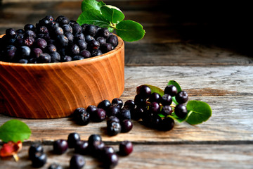 Black chokeberry in wooden utensils on old wooden boards.