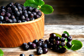 Black chokeberry in wooden utensils on old wooden boards.