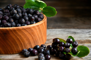 Black chokeberry in wooden utensils on old wooden boards.