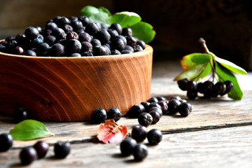 Black chokeberry in wooden utensils on old wooden boards.