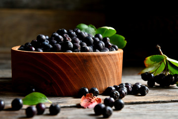 Black chokeberry in wooden utensils on old wooden boards.