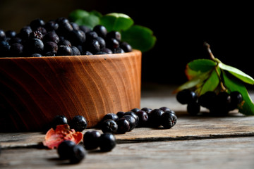 Black chokeberry in wooden utensils on old wooden boards.