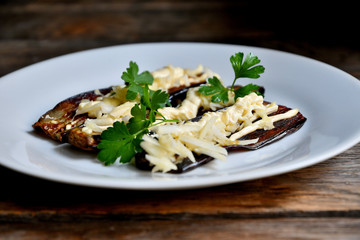 Fried eggplants with parsley, garlic and mayonnaise, in a white plate on a wooden table.