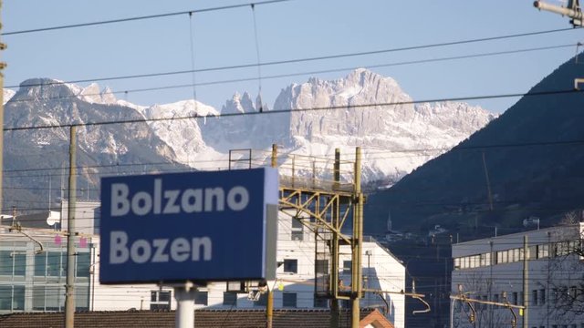 Bolzano train station sign with city name, mountains on the background. Trentino, Italy