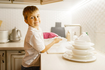 Little boy in gloves washing dishes on the kitchen