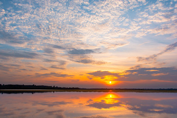 Obraz premium Sunset reflection lagoon. beautiful sunset behind the clouds and blue sky above the over lagoon landscape background. dramatic sky with cloud at sunset