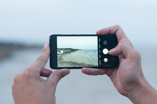 View of the seascape with a cliff through the screen of a smartphone in the hands of man