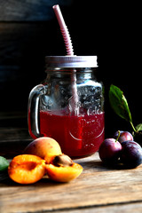Compote of plums and apricots in a glass beaker with a straw on a wooden table.