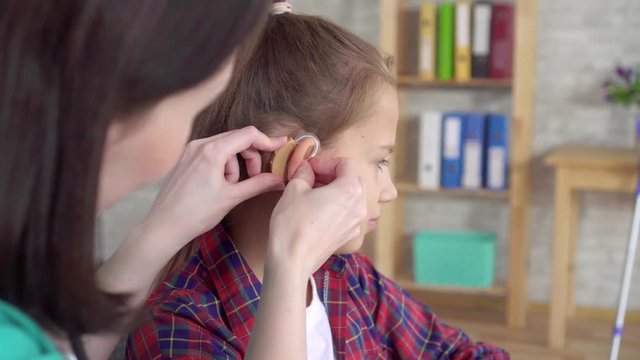 doctor otolaryngologist helps to put on the hearing aid to a hearing impaired teenage girl close up