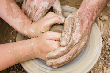 two pairs of hands mold something from clay on a potter's wheel