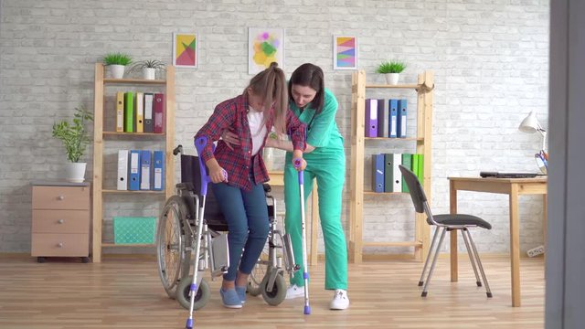 Nurse helps a disabled girl to get up from a wheelchair after an injury