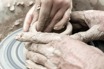 two pairs of hands mold something from clay on a potter's wheel