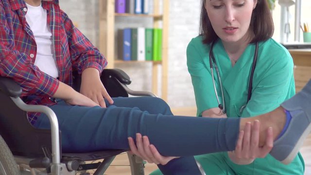 doctor in the clinic examines the leg of a teenage girl with a disability in a wheelchair