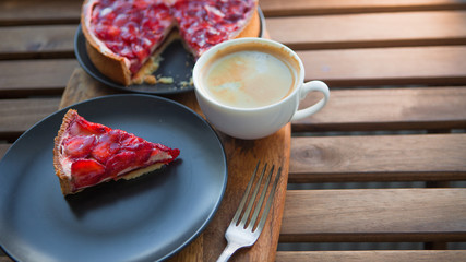 Still life with a Cup of coffee and sweet dessert with strawberries on a wooden table, cheesecake cake with slices of berries in jelly on top.
