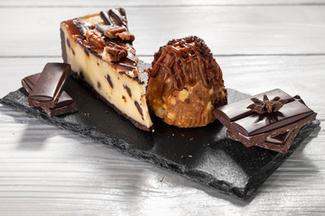 Brownie cheesecake with nuts, chocolate, sweet cake on stone plate on white wooden background.