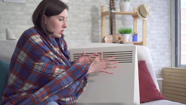 young woman freezes in the living room and heats herself next to an electric heater