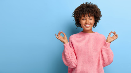 Relaxed charming smiling woman with crisp hair, enjoys mediation, stands in lotus pose, practices...