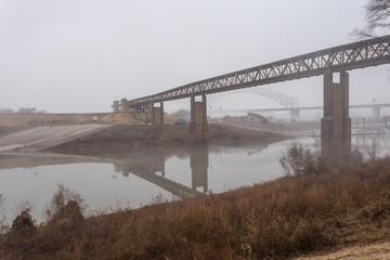 Brown foliage in front of long bridge over Mississippi river