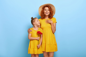 Lovely small girl in yellow polkadot summer dress gives red gerbera flower to her mom, receives...